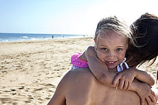 Leende flicka omfamnar sin mamma på stranden