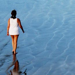 Una signora passeggia sul bagnasciuga della spiaggia