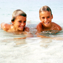 Två leende barn leker på stranden