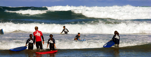 Ragazzi fanno surf insieme all'istruttore sulle loro tavole sul bagnasciuga della spiaggia