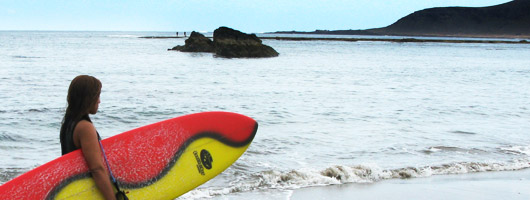 A girl walks along Las Canteras beach with her surf board