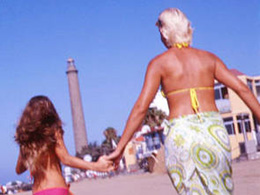 Mor och dotter springer på stranden i Maspalomas med fyren i bakgrunden