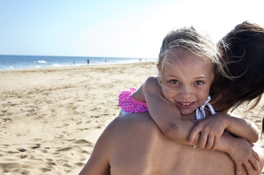 A girl smiles and hugs her mother on the beach