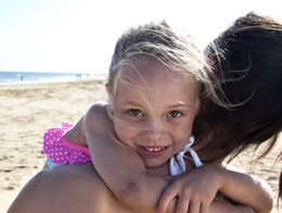 Dziewczynka uśmiecha się tuląc się do mamy na plaży