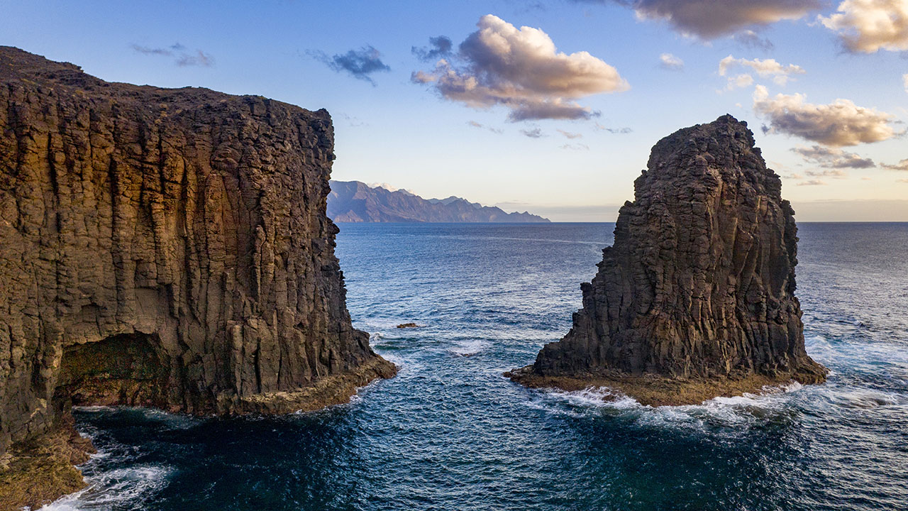 Andén Verde, también conocido como la Cola de Dragón, al fondo de la imagen. Roque Farallón o Roque Partido en la costa de Gáldar en primer plano de la foto. 