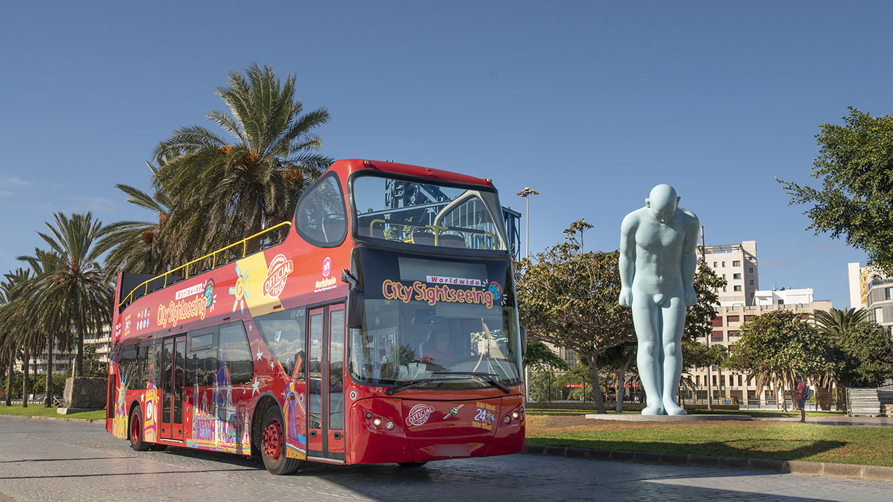 A tourist bus parked next to the Greetingman sculpture in Plaza de Canarias