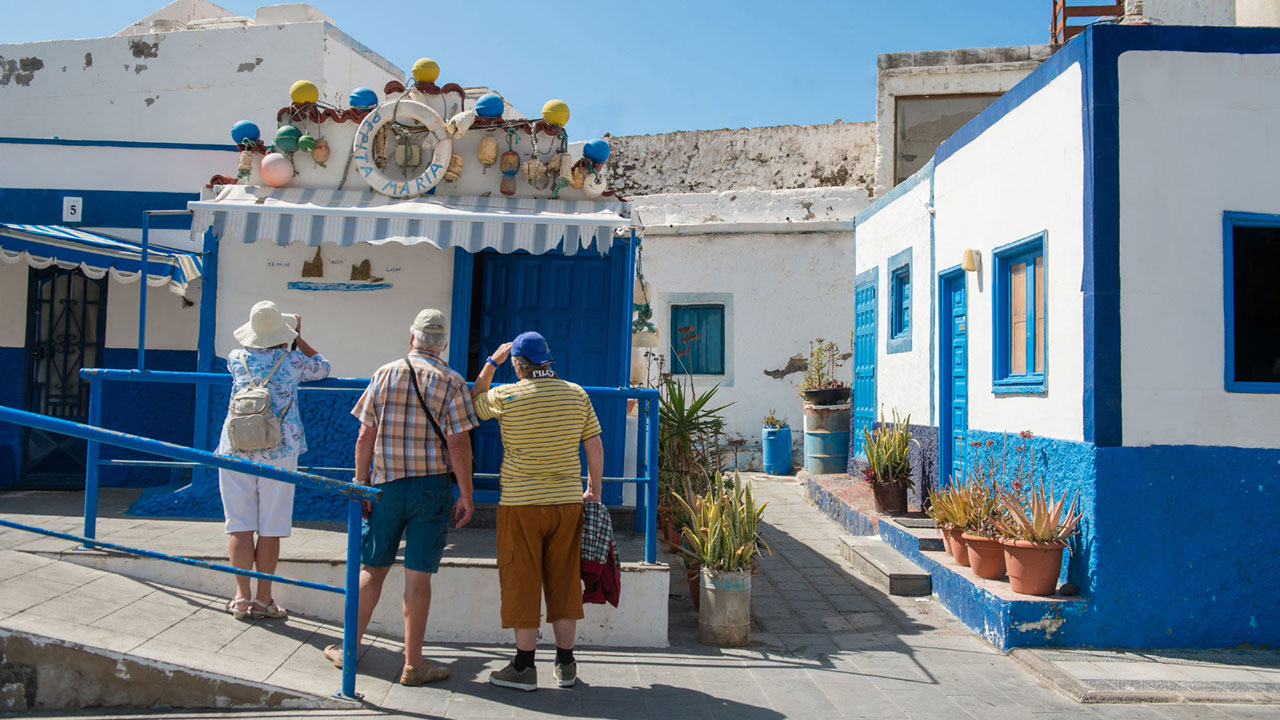 Eine Gruppe von Besuchern beobachtet und photographiert die kleine weiss und blau Häuser von Agaete, Gran Canaria