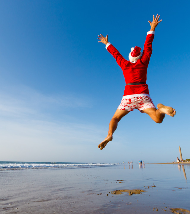 A man who is wearing like a Santa Claus jumps in Maspalomas beach, Gran Canaria