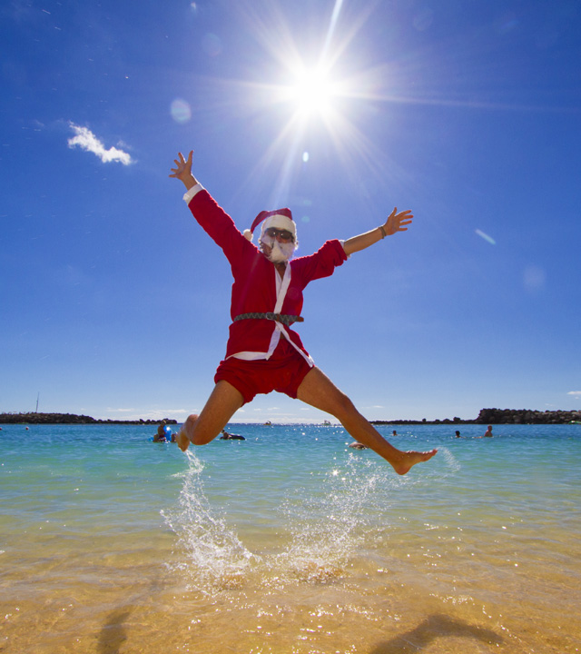 A man who is wearing like a Santa Claus jumps in Amadores beach, Gran Canaria