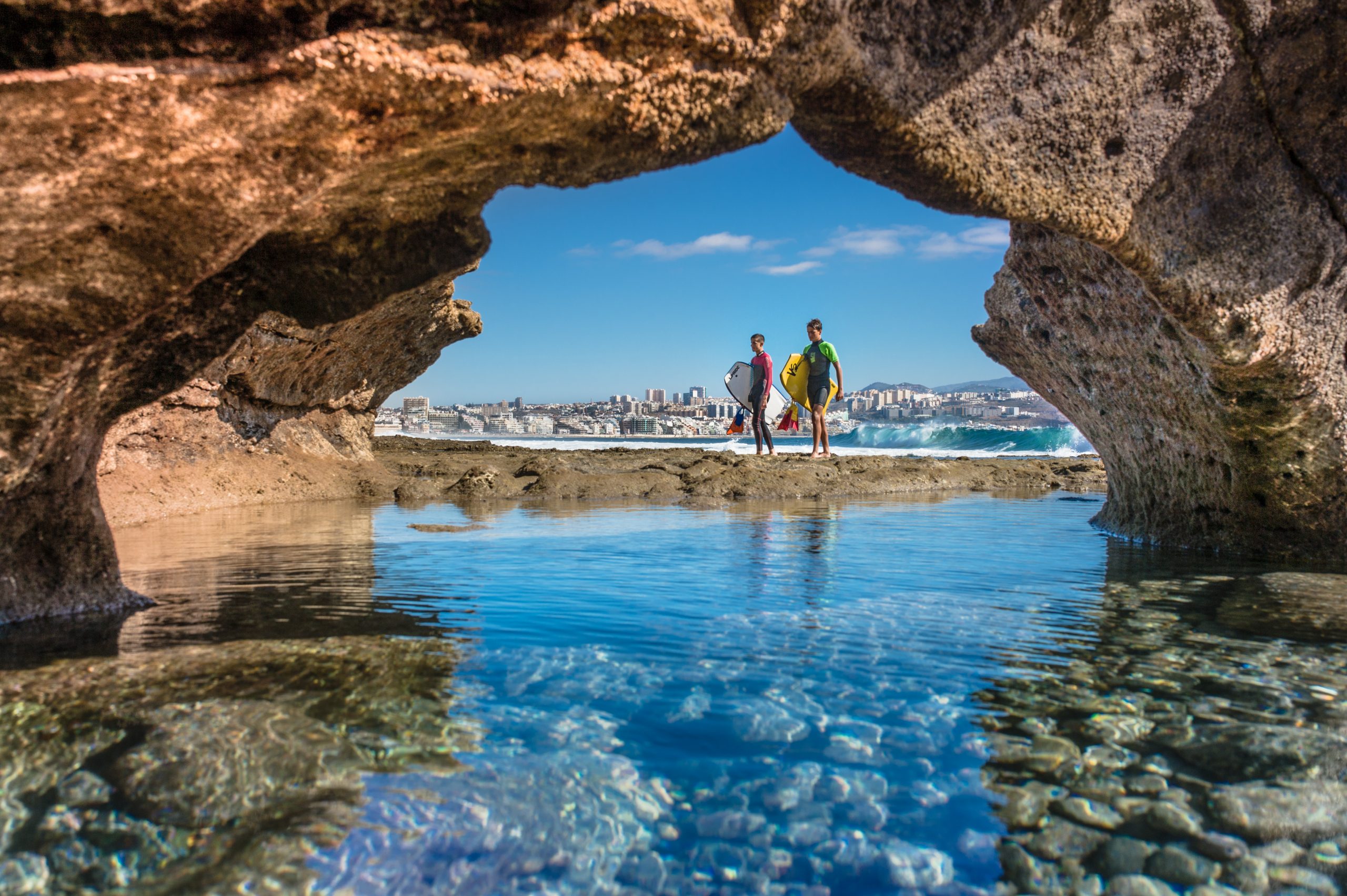 Foto de jovenes surferos vistos desde un hueco en la roca en la bahía de El Confital