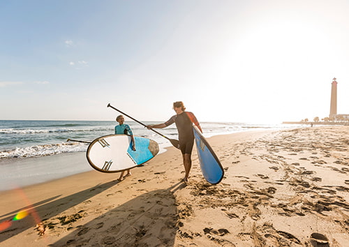 Pareja paseando por la playa con tablas de paddle surf