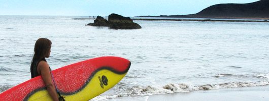 Una ragazza passeggia con la sua tavola sulla spiaggia di Las Canteras