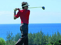 A golfer practising his drive with the sea in the background